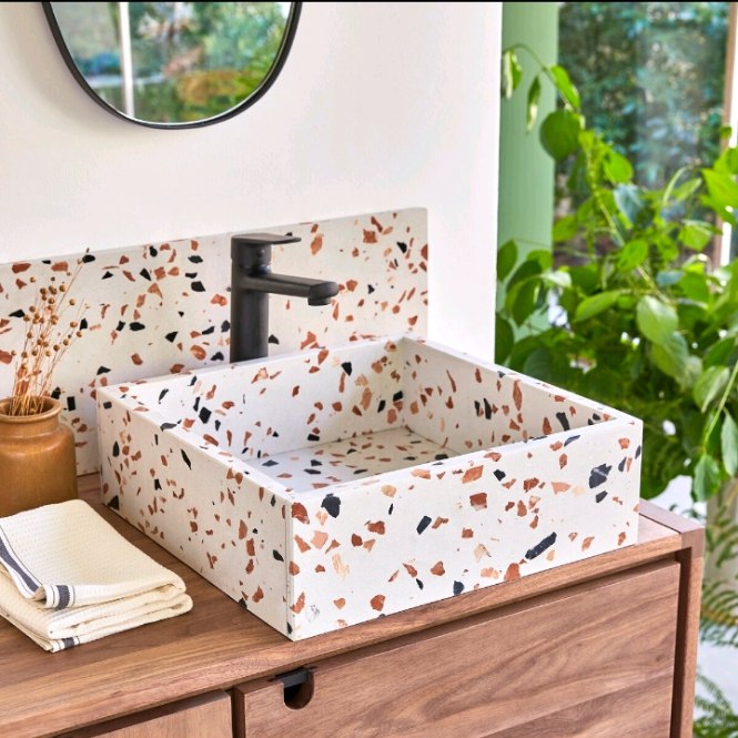 Vanity kayu dengan wastafel terazzo putih bermotif chip warna hangat dan tanaman hijau